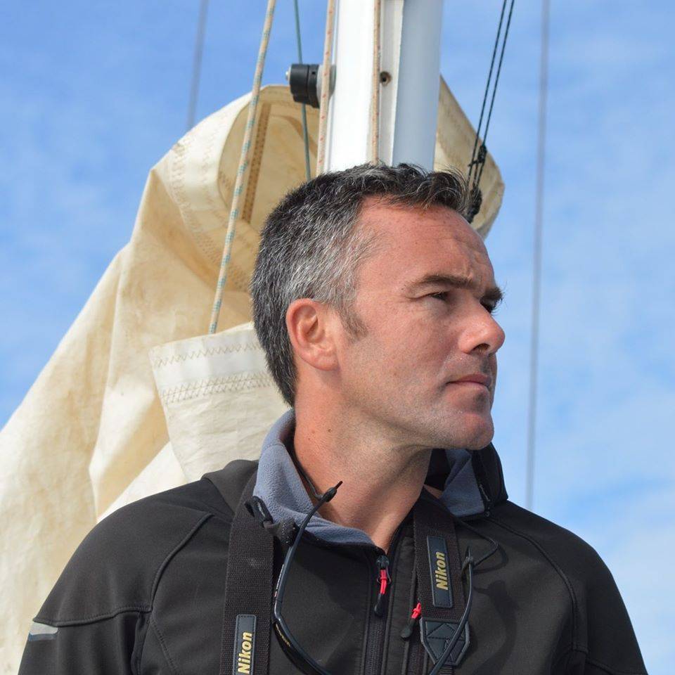 a man standing on a sailboat looking at the sky.