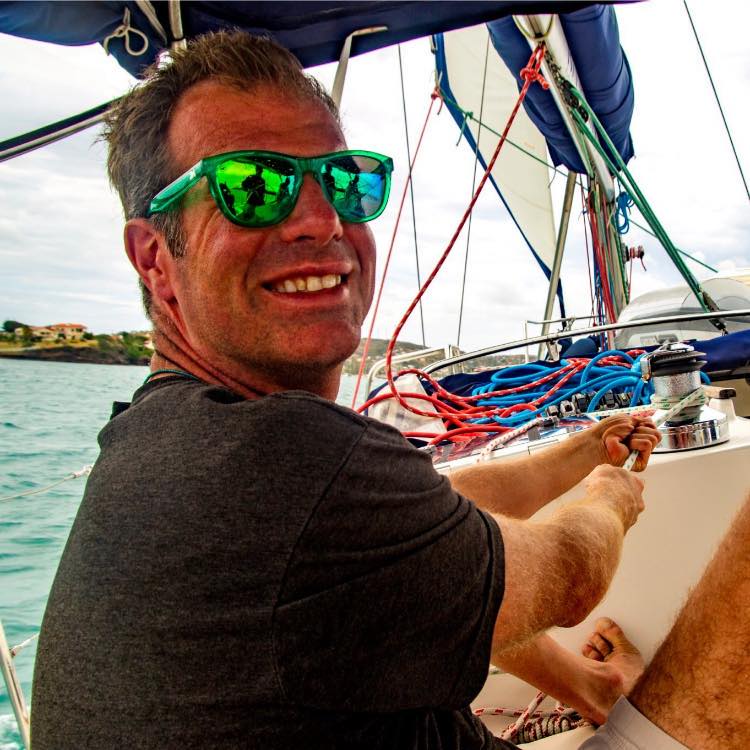 a man wearing sunglasses sitting on a sailboat.