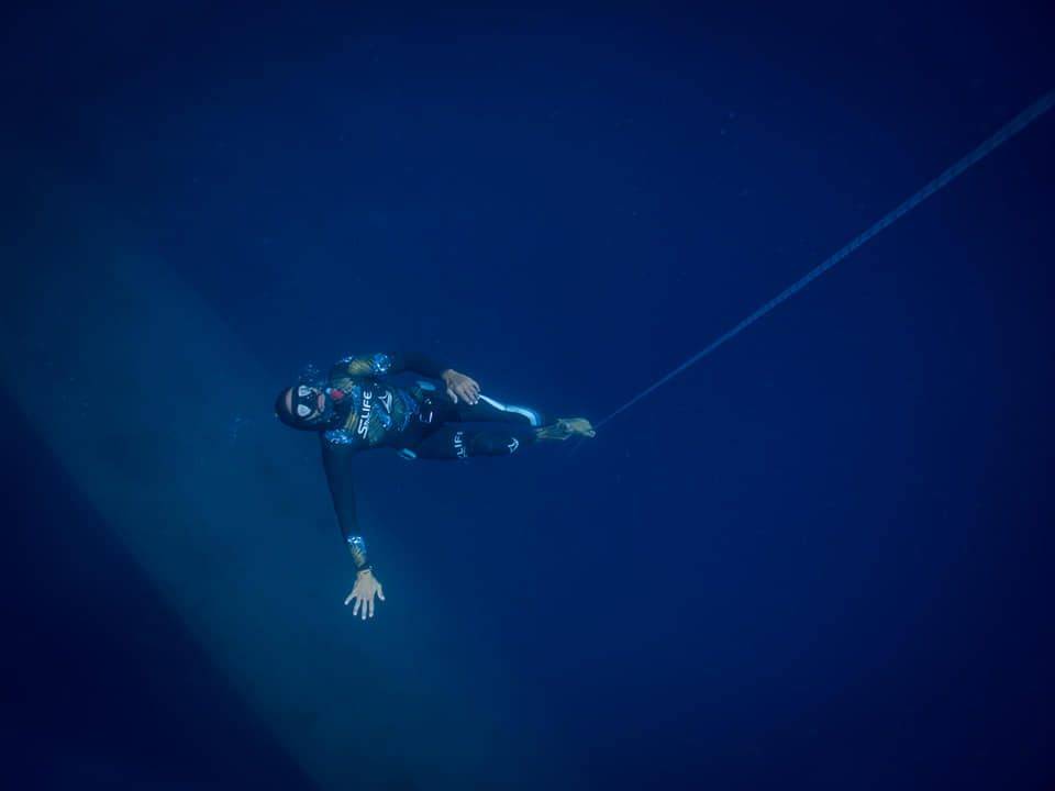 a scuba diver in a wetsuit hanging from a rope.
