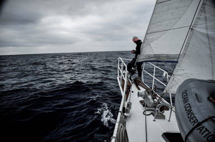 a man is standing on the bow of a sailboat in the ocean.
