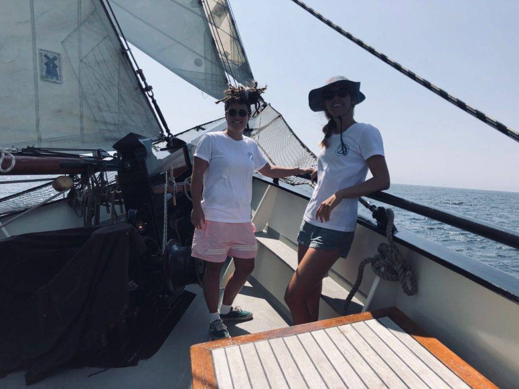 two people standing on the deck of a sailboat.