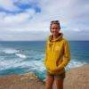 A woman in an Ocean Nomads Hoodie - Unisex standing on a cliff overlooking the ocean as part of the Ocean Nomads community.