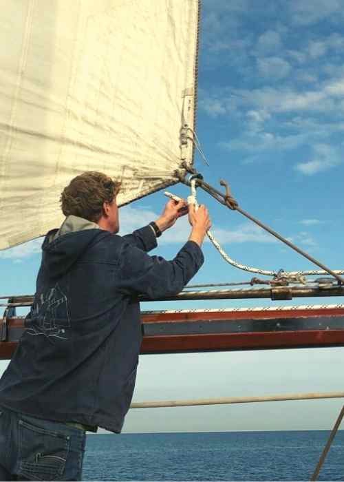 A man from an offshore sailing crew is working on the sail of a sailboat.