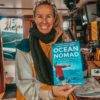 a woman holding up a book called ocean nomad.