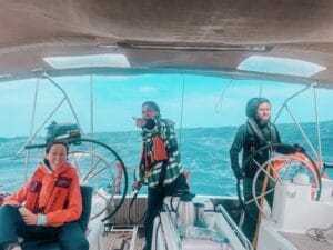 Three people navigating a boat on the ocean near Cape Verde. Two are steering the wheels while one confidently points ahead. Dressed in life jackets, they embrace the adventure, undeterred by the slightly choppy sea under a cloudy sky.
